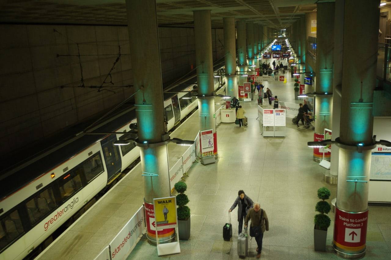 Passengers with luggage on the concourse at Stansted Airport railway station, with signs to the London train platforms